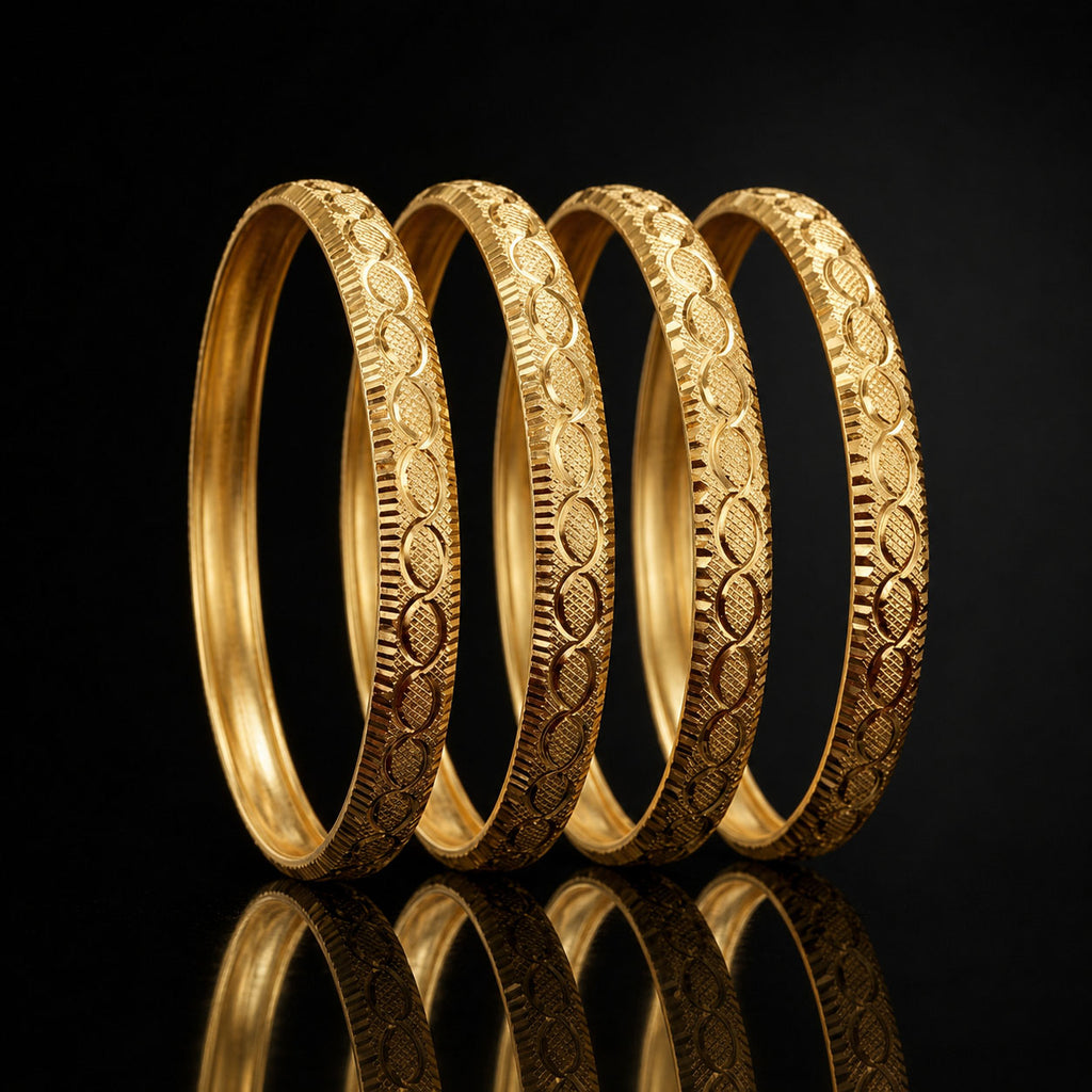 Four gold-toned bangles with detailed floral and geometric engravings, arranged in a row on a reflective black surface.
