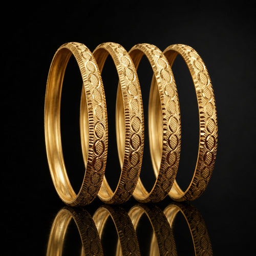 Four gold-toned bangles with detailed floral and geometric engravings, arranged in a row on a reflective black surface.