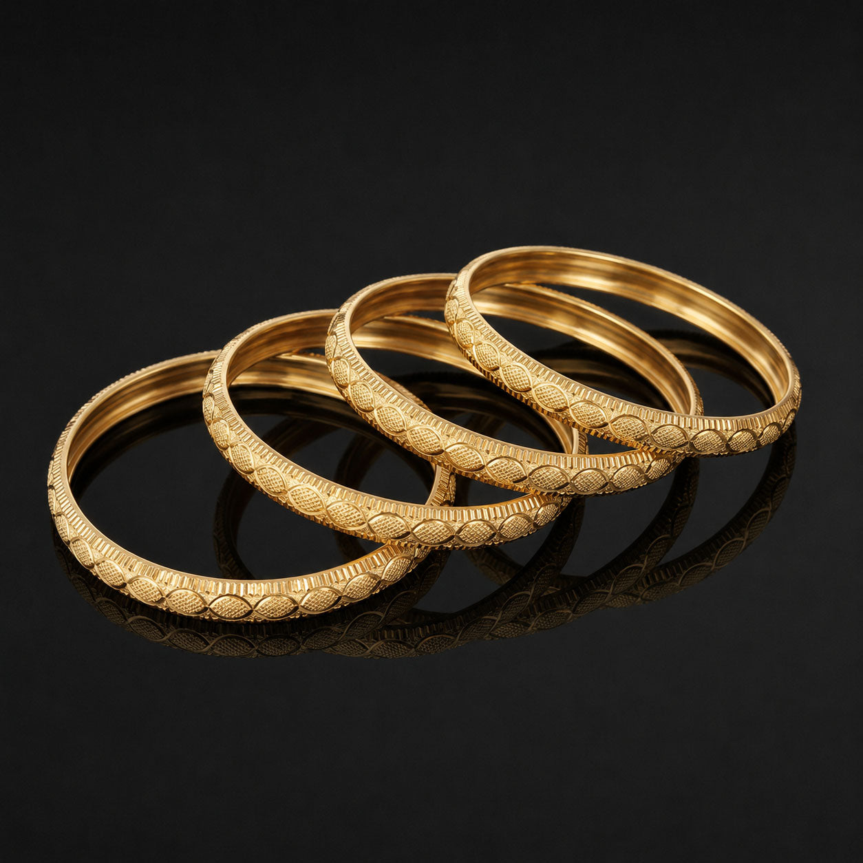 Four gold-toned bangles with detailed textured patterns, arranged in an overlapping fan shape on a reflective black surface.