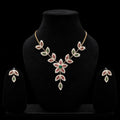 A gold-toned jewelry set displayed on a black velvet mannequin bust, featuring a leafy floral necklace with red and green stones, matching drop earrings, and a black background.