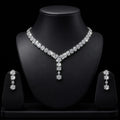 A sparkling silver-tone jewelry set displayed on a black mannequin bust, featuring a V-necklace with a matching drop pendant and two matching drop earrings on small display stands against a black background.