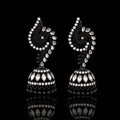 A pair of ornate black and silver jhumka earrings with intricate paisley and floral motifs, displayed on a reflective black surface.