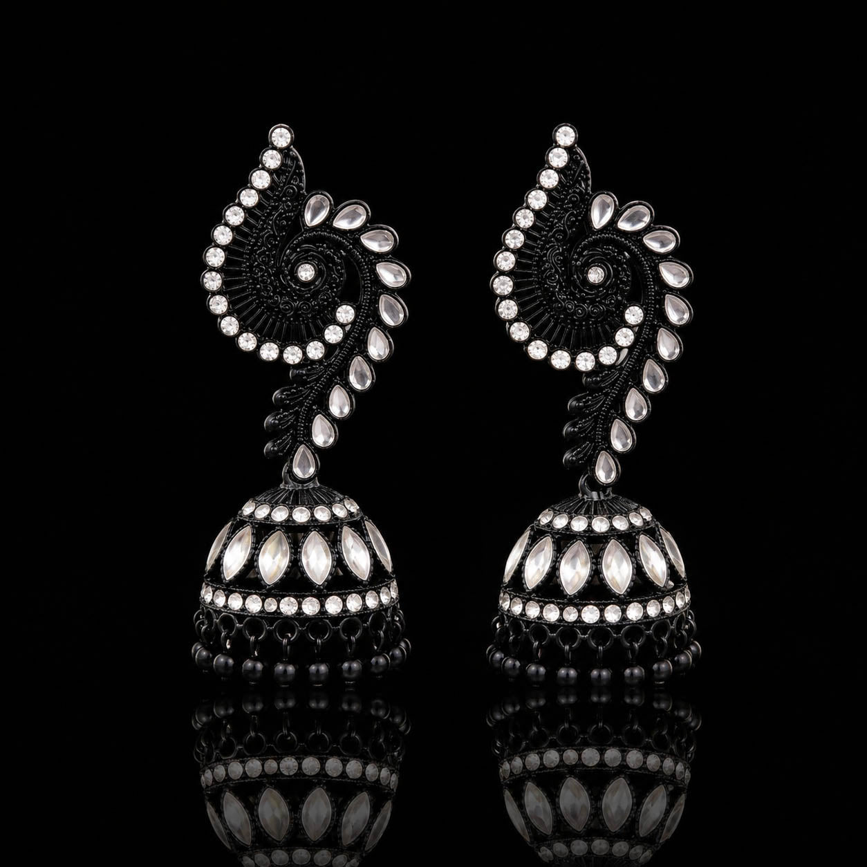 A pair of ornate black and silver jhumka earrings with intricate paisley and floral motifs, displayed on a reflective black surface.