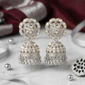 Silver jhumka earrings on a marble surface with small silver balls.