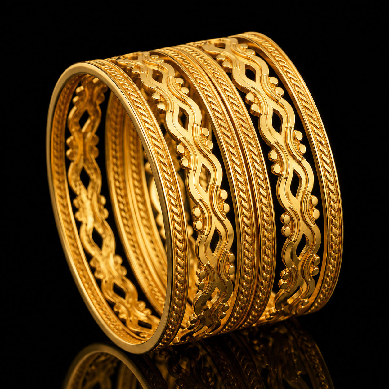 A stack of five wide gold bangles with intricate woven and floral patterns, displayed on a reflective black surface.