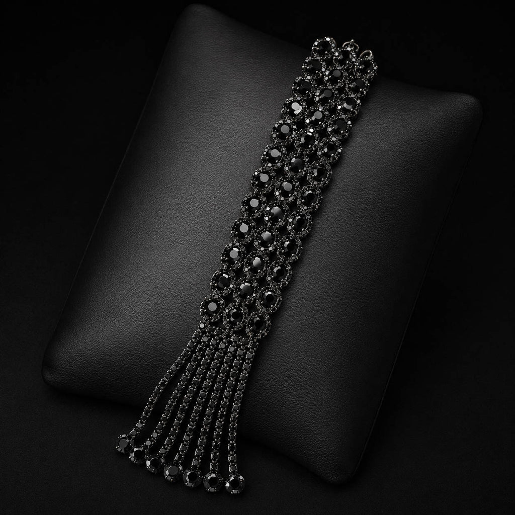 A black beaded tassel bracelet displayed on a black textured cushion against a dark background.