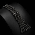 A black gemstone choker necklace displayed on a black jewelry bust, featuring a wide top band with a cascading fringe of smaller dangling chains.
