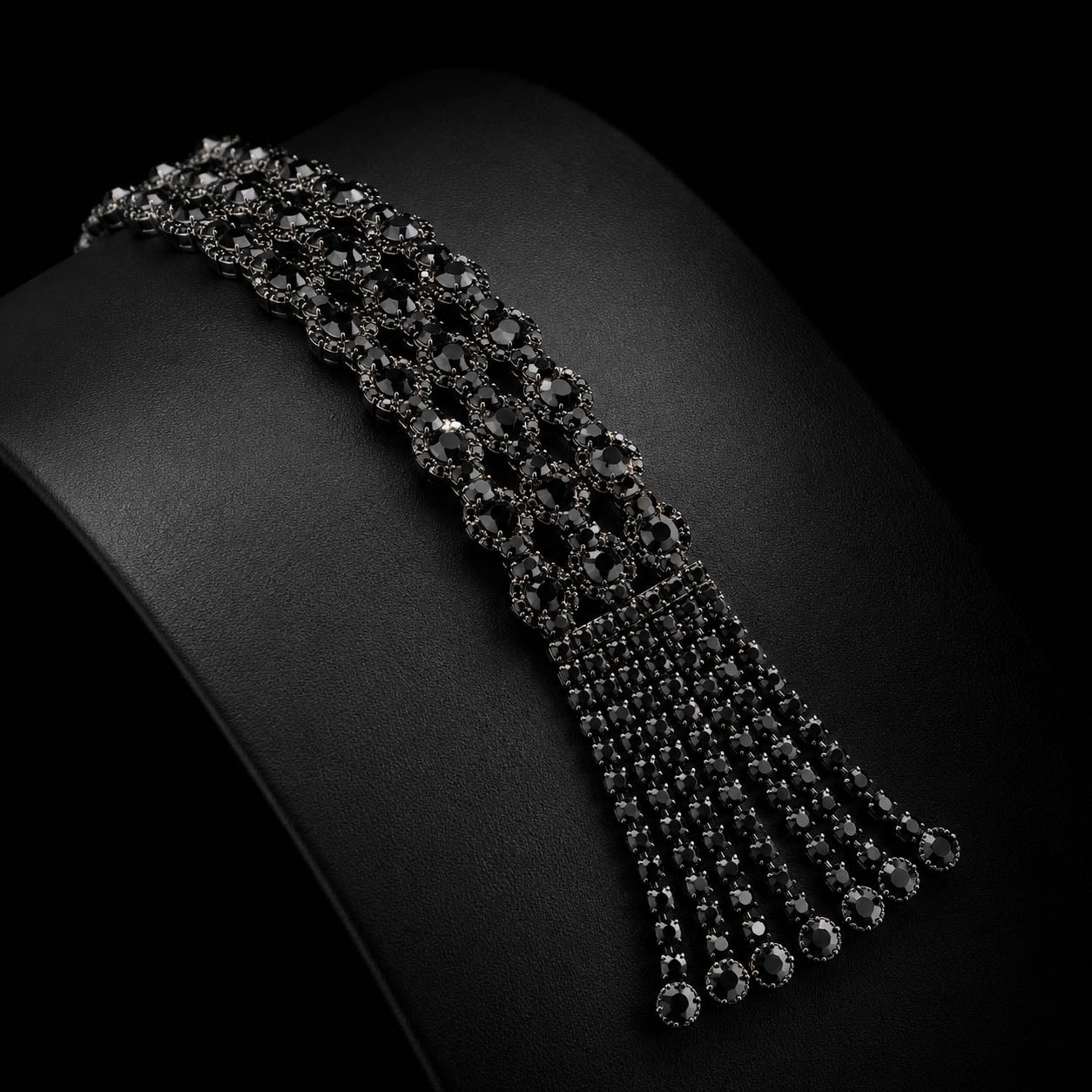 A black gemstone choker necklace displayed on a black jewelry bust, featuring a wide top band with a cascading fringe of smaller dangling chains.