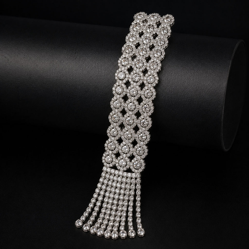 A silver-toned statement bracelet featuring a wide band of repeating floral clusters and a dangling fringe, displayed on a black cylindrical stand.