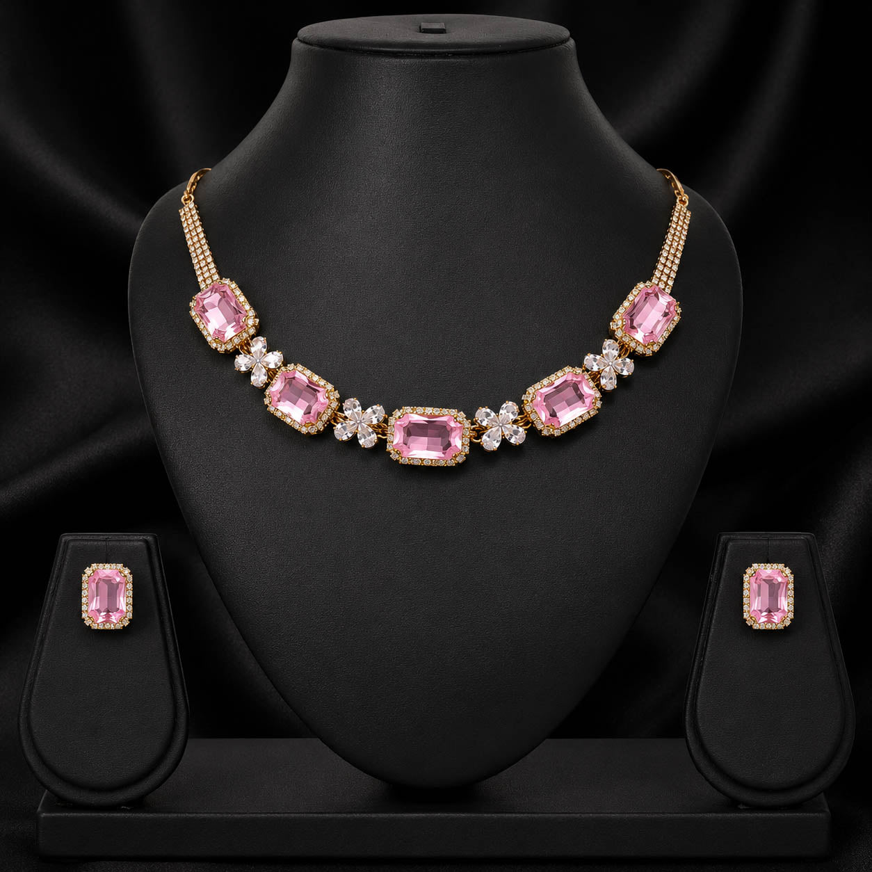 Gold-plated pink gemstone necklace and matching stud earrings displayed on a black jewelry bust against a black satin background.