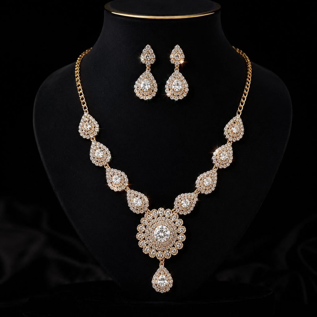 Gold-plated jewelry set featuring a statement necklace and matching teardrop earrings, both adorned with clear rhinestones, displayed on a black velvet mannequin bust.