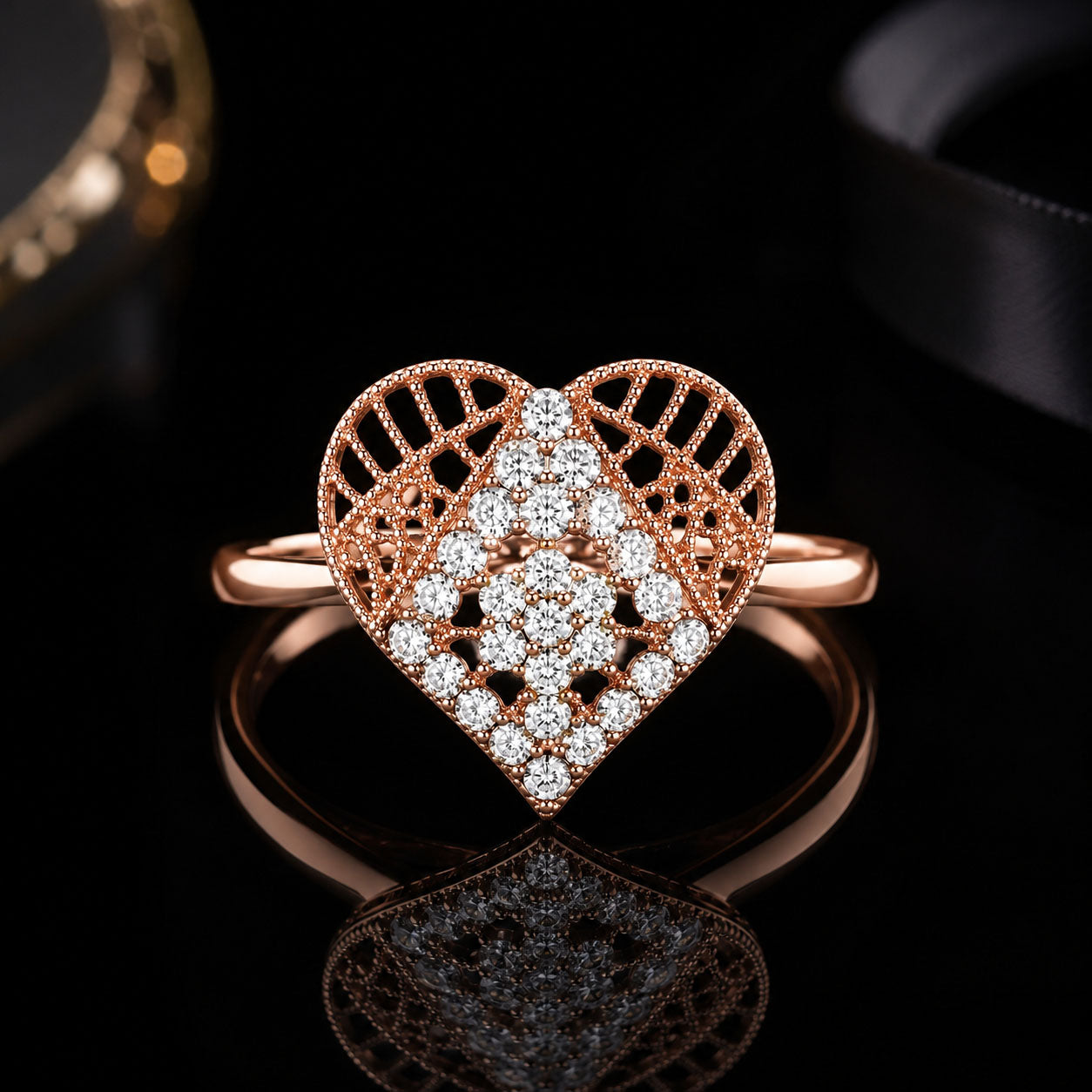 A heart-shaped rose gold ring with pavé diamonds, displayed on a reflective black surface with a dark background.
