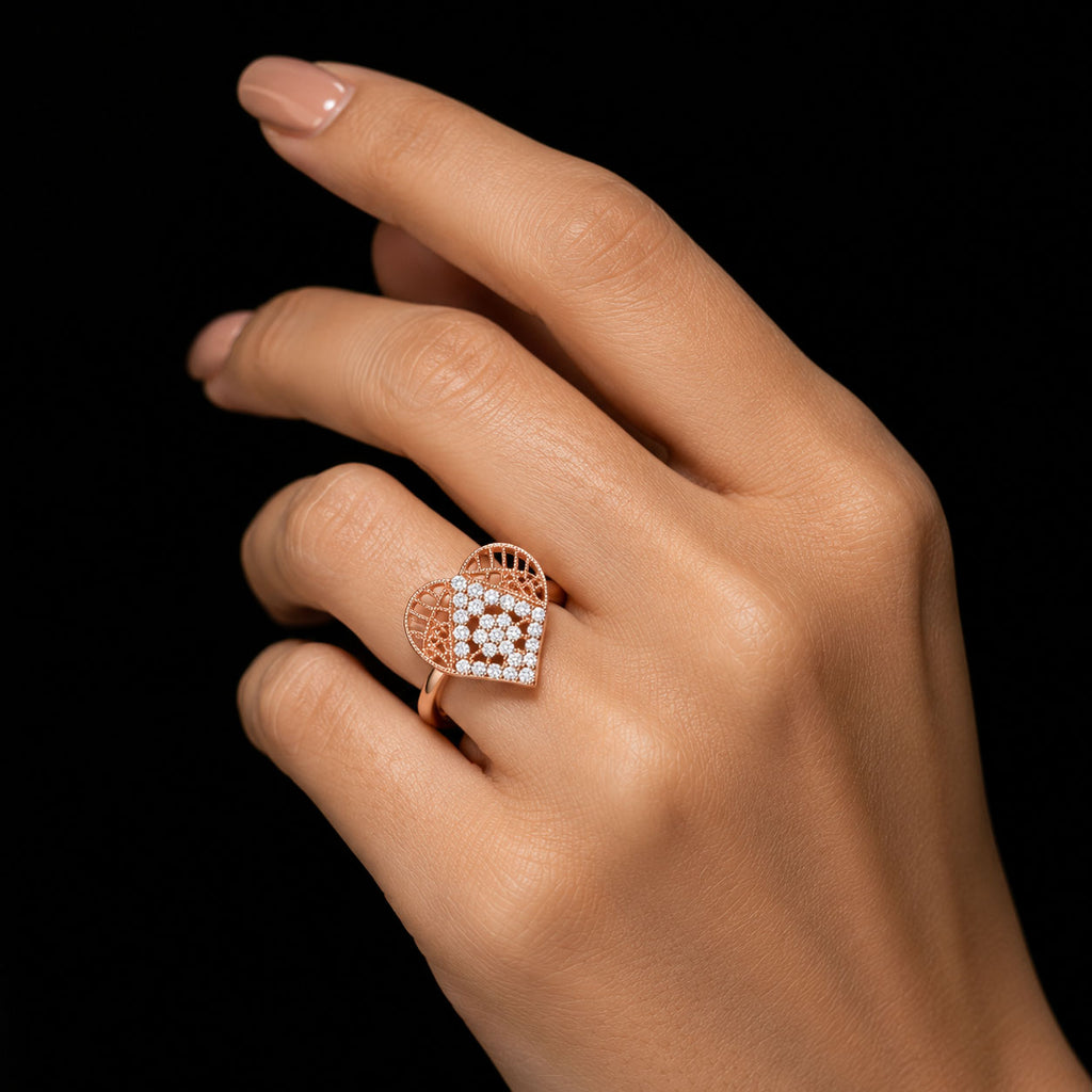 A close-up of a hand wearing a rose gold ring with a heart-shaped pavé diamond setting, shown against a solid black background.
