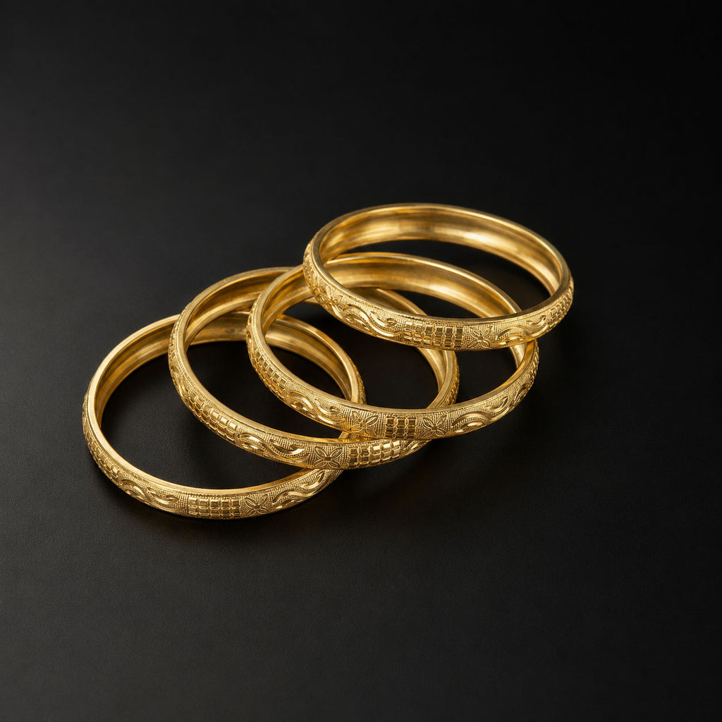 Four gold bangles with detailed floral and geometric engravings, arranged in a cascading stack on a dark black background.