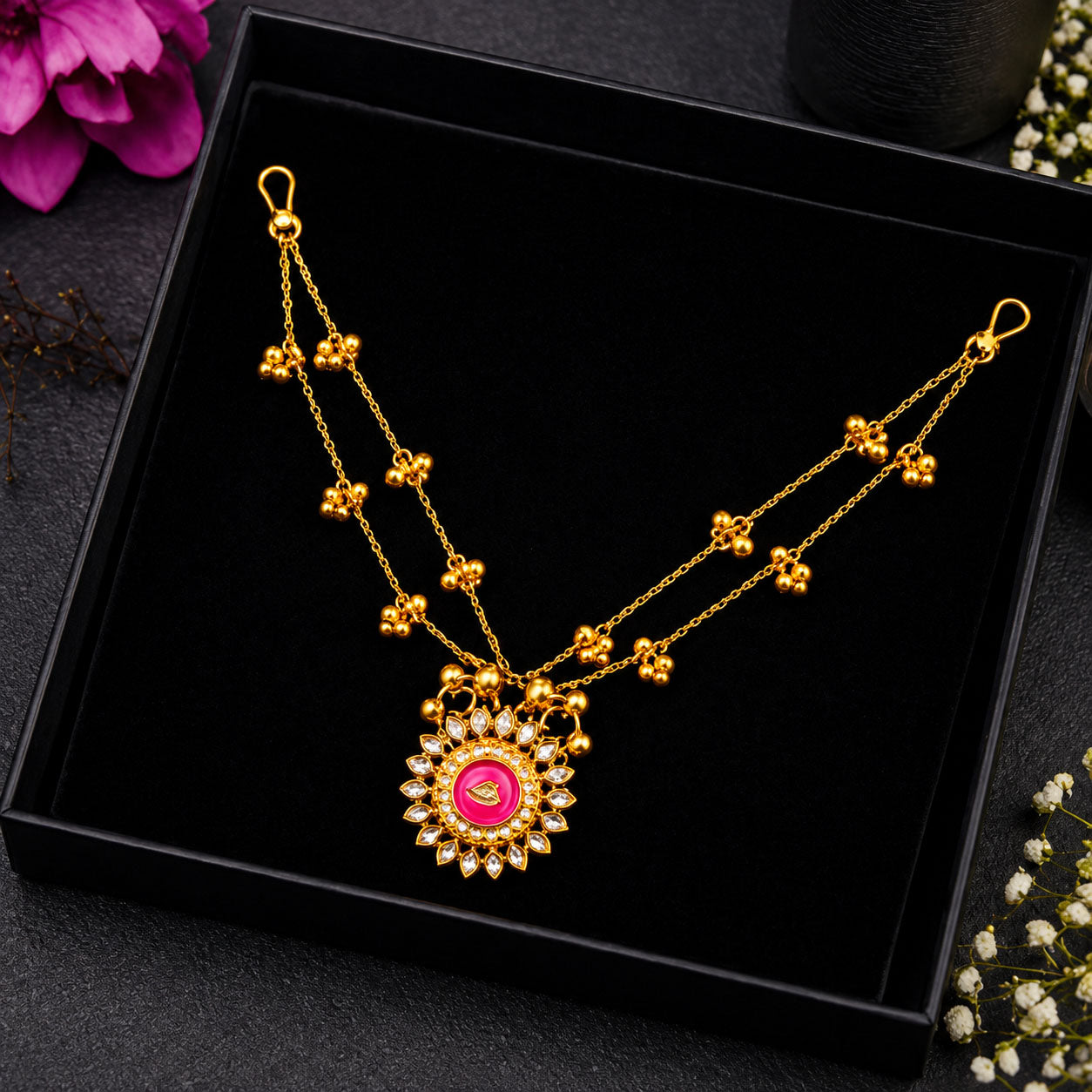 A gold double-strand necklace with a circular pink pendant, displayed inside a black presentation box.