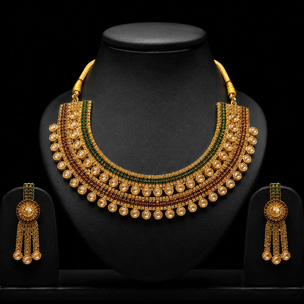 Gold-plated traditional Indian statement necklace and matching drop earrings displayed on a black mannequin bust and stand against a black background.