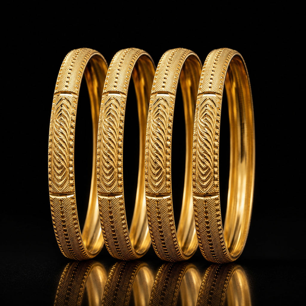Four gold bangles with detailed geometric and chevron patterns, arranged in a row on a reflective black surface against a black background.