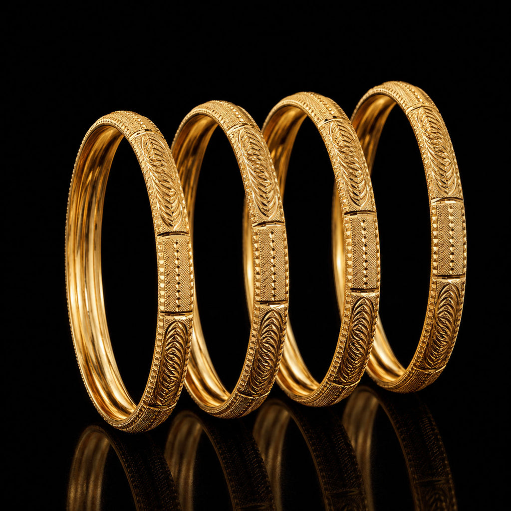 Four gold-toned bangles with detailed engraved patterns, arranged in a row against a solid black background with a reflective surface below.