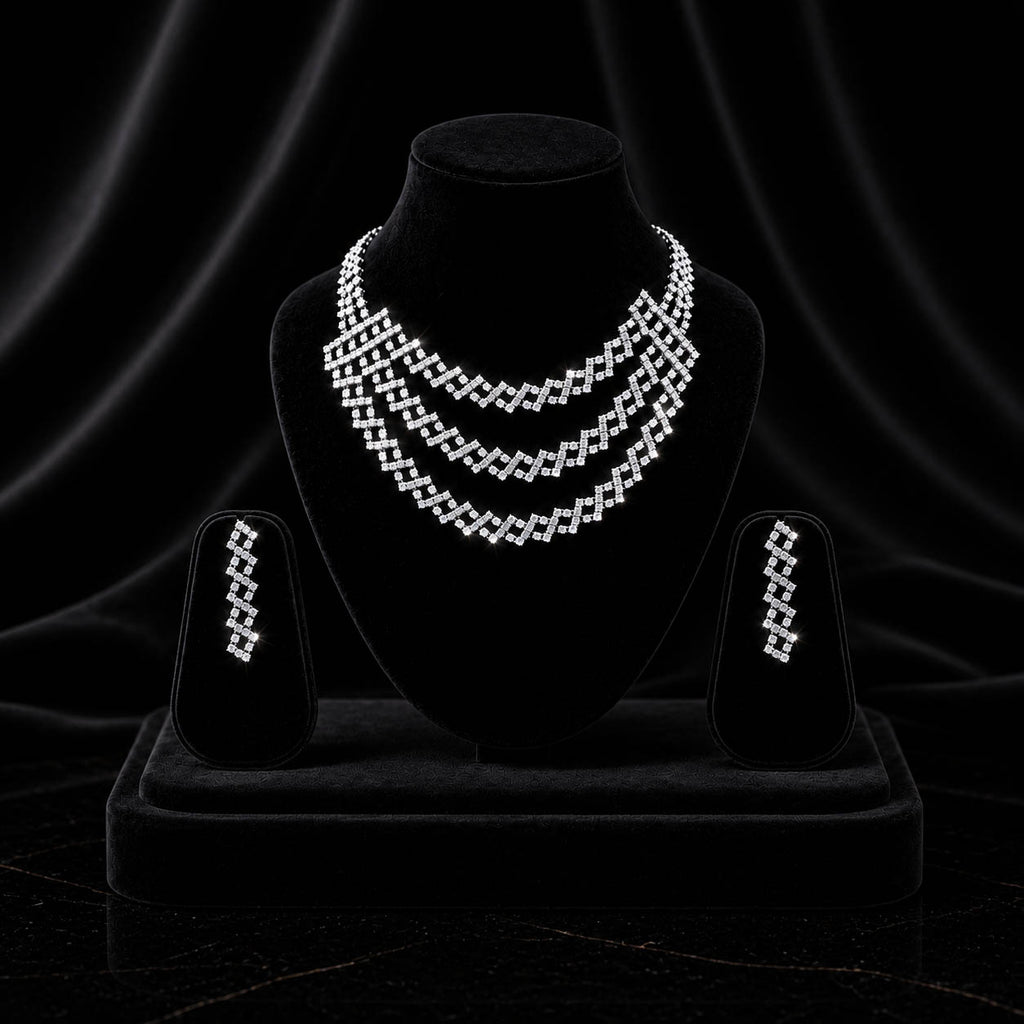 A three-piece silver jewelry set featuring a multi-strand geometric necklace, a matching drop earrings, and a ring, all displayed on black velvet jewelry stands against a dark draped background.