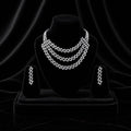 A three-piece silver jewelry set featuring a multi-strand geometric necklace, a matching drop earrings, and a ring, all displayed on black velvet jewelry stands against a dark draped background.